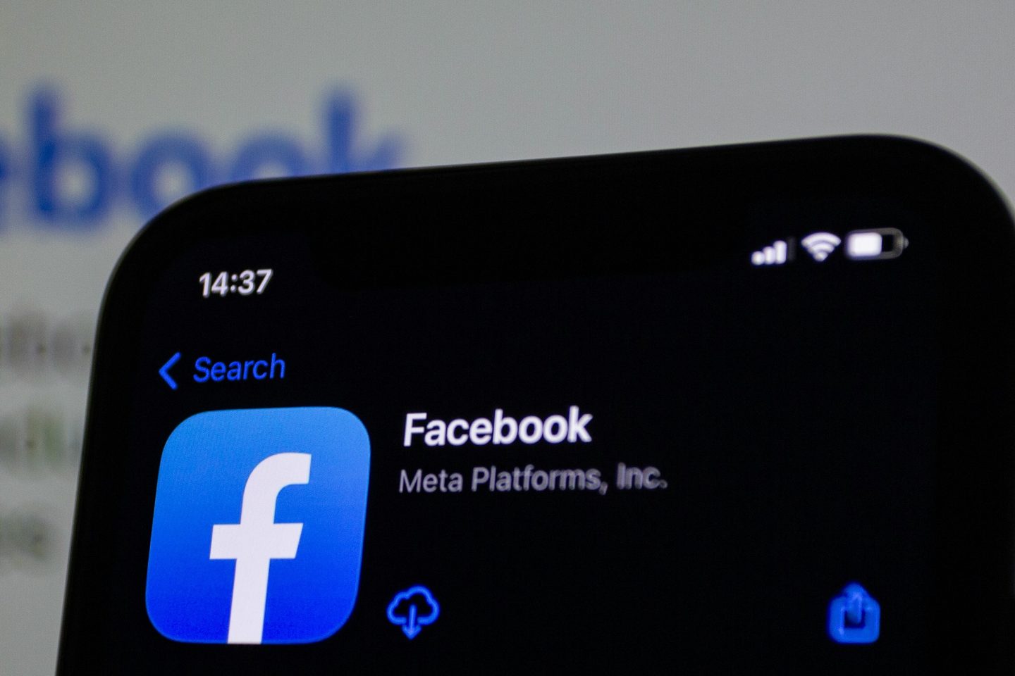Smartphone affichant la fiche de l'application Facebook dans l'App Store, devant le logo Facebook flou.