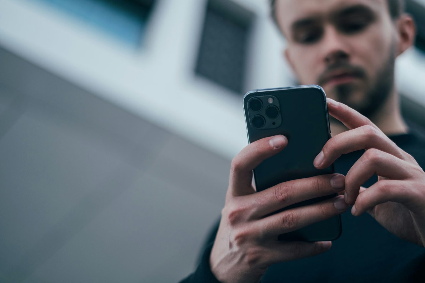 Un homme regarde l'écran de son smartphone, photographié en contre-plongée.