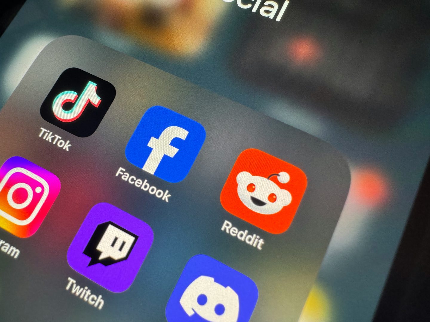 Gros plan sur l'écran d'un smartphone : dossier « Social » avec les icônes de TikTok, Facebook, Reddit, Instagram, Twitch et Discord.