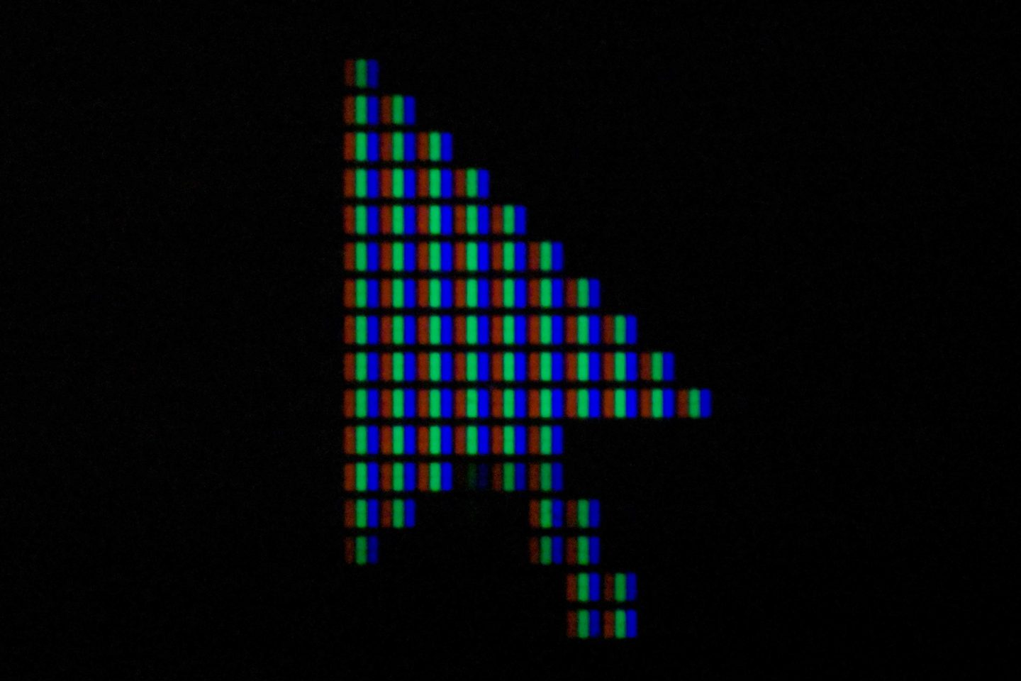 Pointeur de souris en forme de flèche vu en très gros plan sur un écran : les sous-pixels verts et bleus dessinent la flèche sur fond noir.